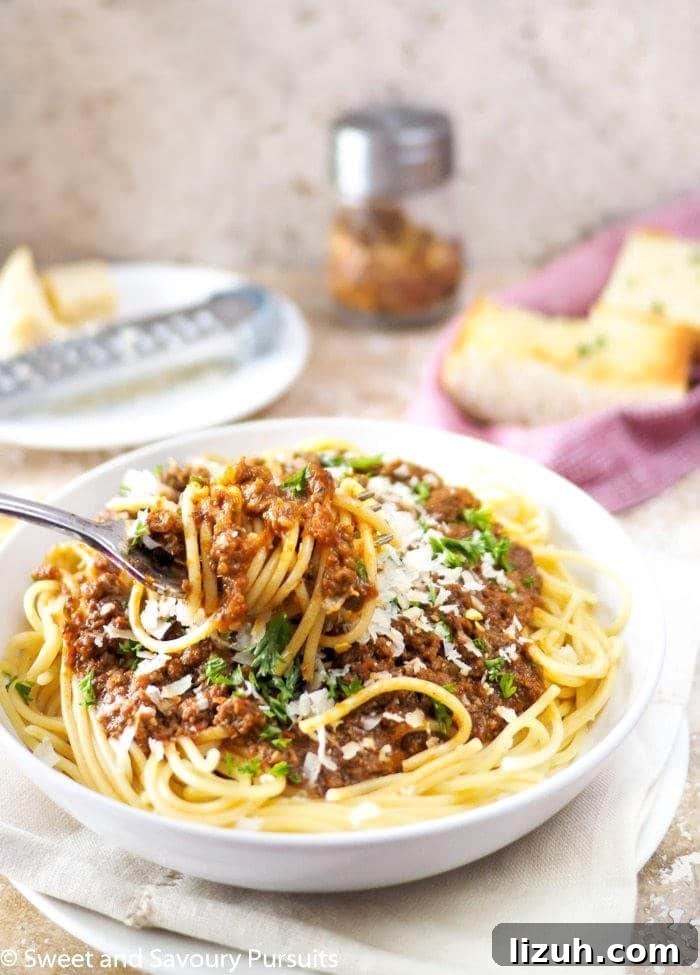Classic Spaghetti with Savory Meat Sauce Recipe 3 Close-up of spaghetti and meat sauce twirled around a fork. Garlic bread in background.