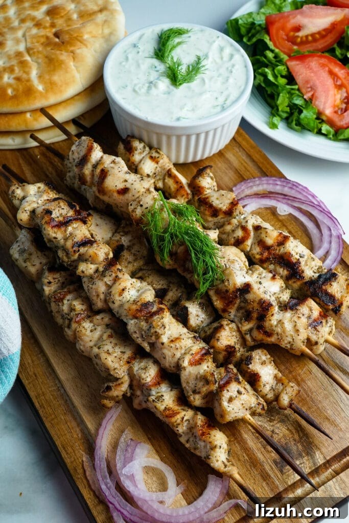 Authentic Greek Chicken Souvlaki Recipe with Tzatziki and Pita 2 Stack of cooked chicken souvlaki on wooden skewers next to a bowl of tzatziki sauce.