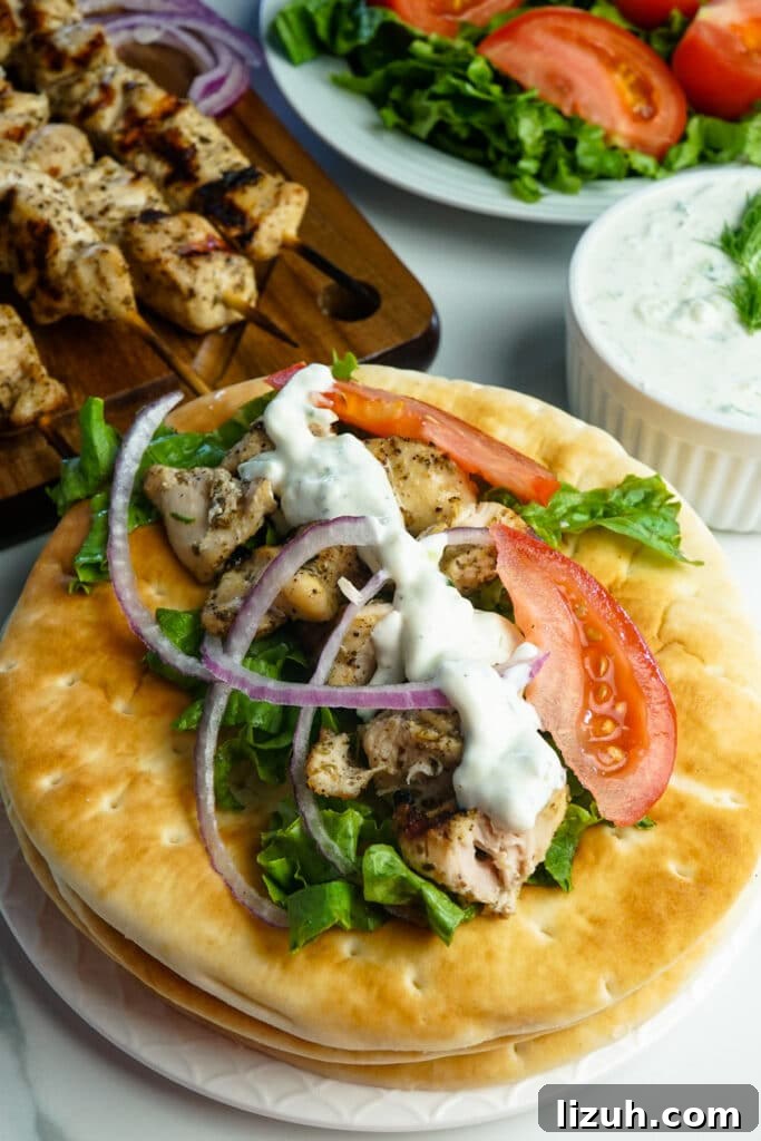 Authentic Greek Chicken Souvlaki Recipe with Tzatziki and Pita 6 Chicken souvlaki with tomatoes, red onions, lettuce, and tzatziki sauce on a stack of warm pita bread.