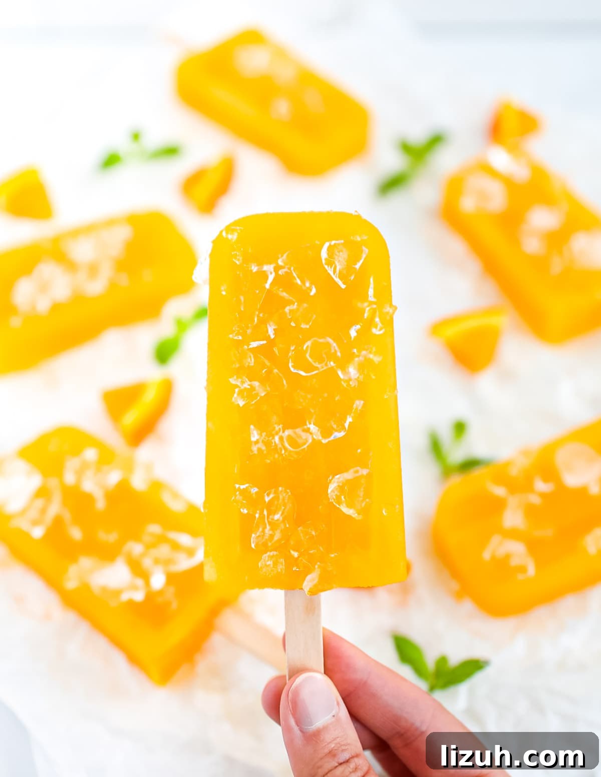 Homemade Orange Popsicles: Refreshing Citrus Ice Pops Recipe 6 A hand holding an orange-yellow ice pop covered in ice