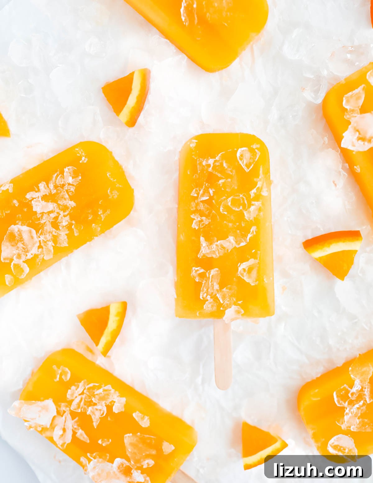 Homemade Orange Popsicles: Refreshing Citrus Ice Pops Recipe 7 Overhead shot of six popsicles covered in crushed ice and surrounded by orange slices