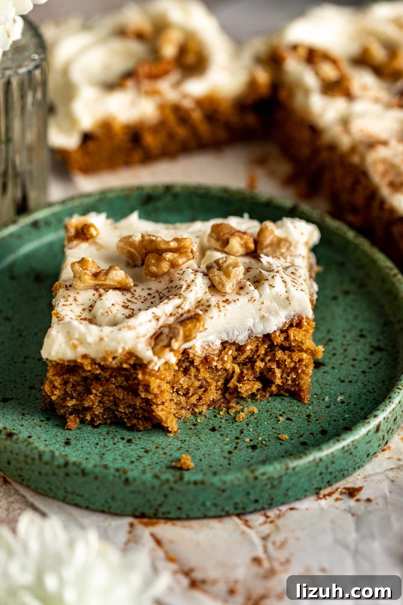 Chewy Carrot Cake Bars with Cream Cheese Frosting Recipe 11 Close-up of a carrot cake bar with a bite taken out, revealing moist crumb texture, cream cheese frosting, and walnut topping.