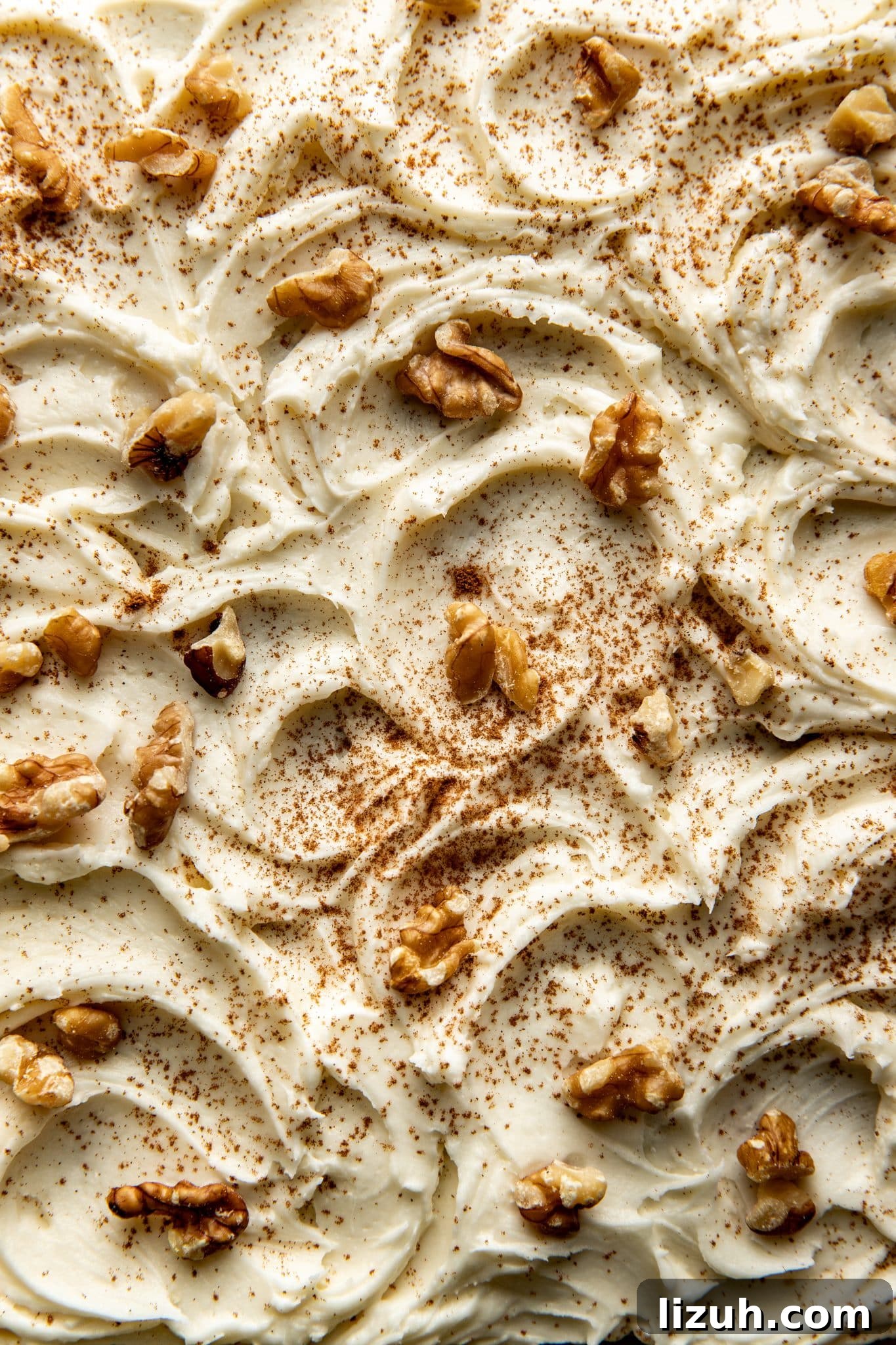 Chewy Carrot Cake Bars with Cream Cheese Frosting Recipe 4 Close-up of creamy cream cheese frosting swirled over carrot cake bars, topped with walnut pieces and a dusting of cinnamon.