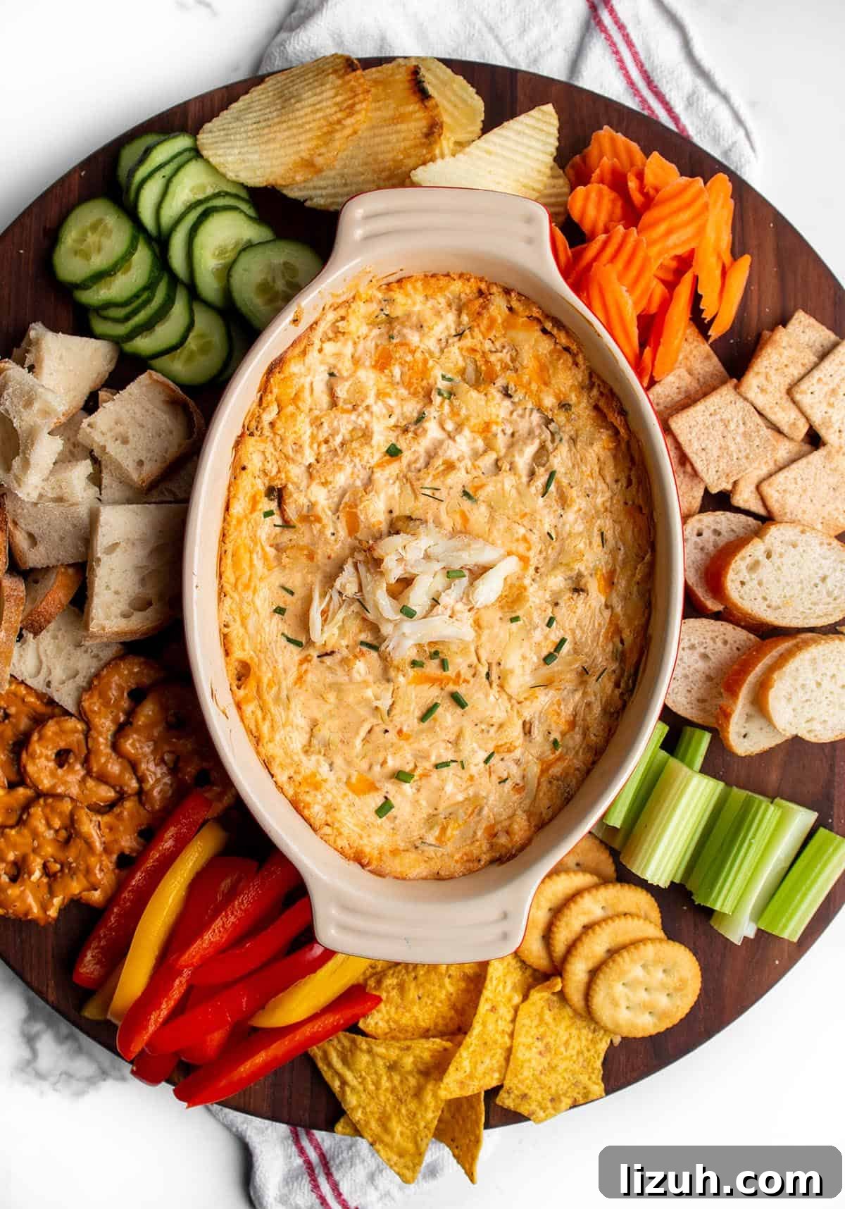 25 Perfect Pairings to Serve with Crab Dip 2 A large circular wood board with a hot crab dip in the middle with fresh produce, bread, chip and crackers around the dish.