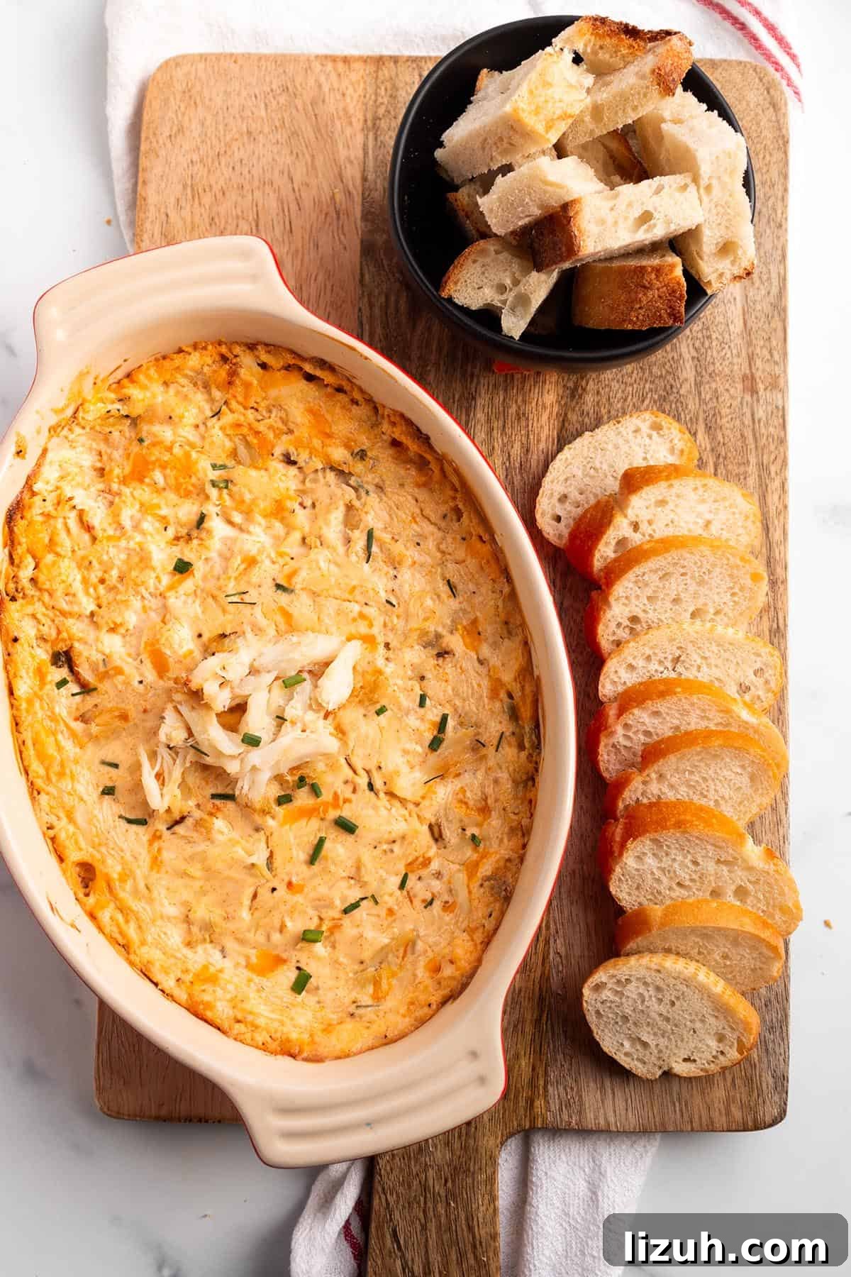 25 Perfect Pairings to Serve with Crab Dip 4 A wooden board with crab dip in a baking dish with sliced baguette and pieces of sourdough.
