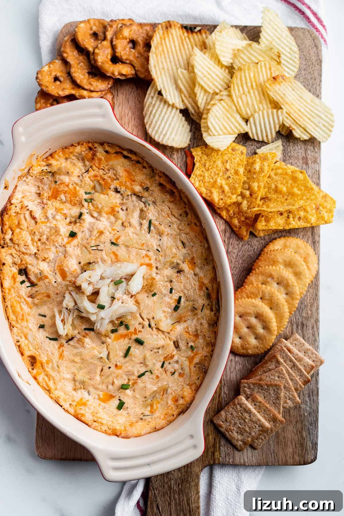 25 Perfect Pairings to Serve with Crab Dip 5 A wooden serving board with a baking dish with crab dip with pretzels, chips and crackers.