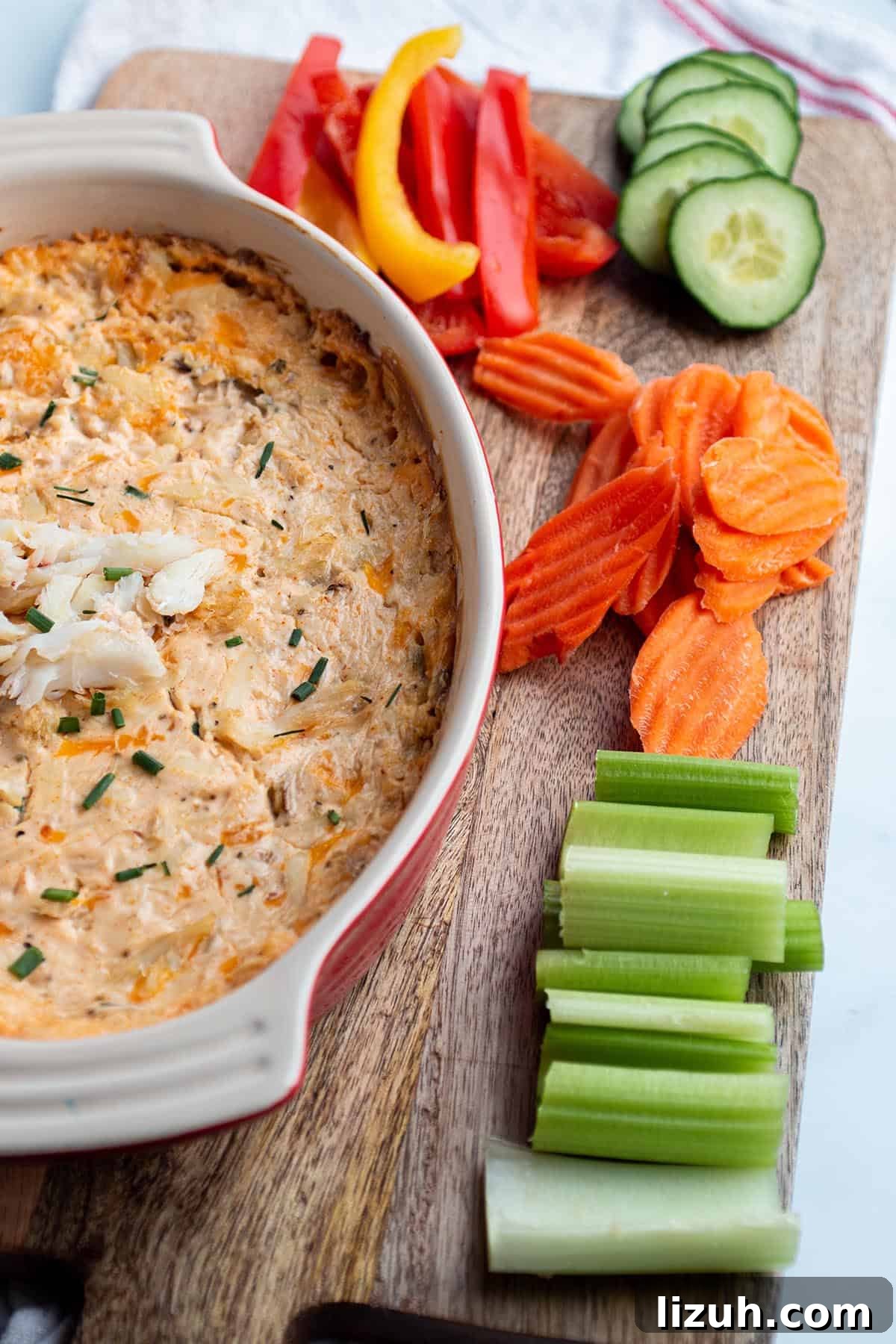 25 Perfect Pairings to Serve with Crab Dip 6 A wooden board with a baking dish full of crab dip with celery, carrots, bell peppers, and cucumber slices.