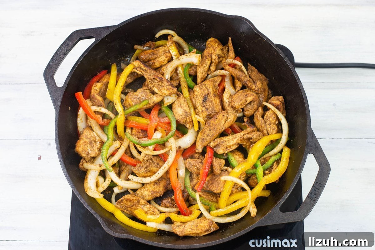 Cooked chicken, bell peppers, and onions in a iron skillet.