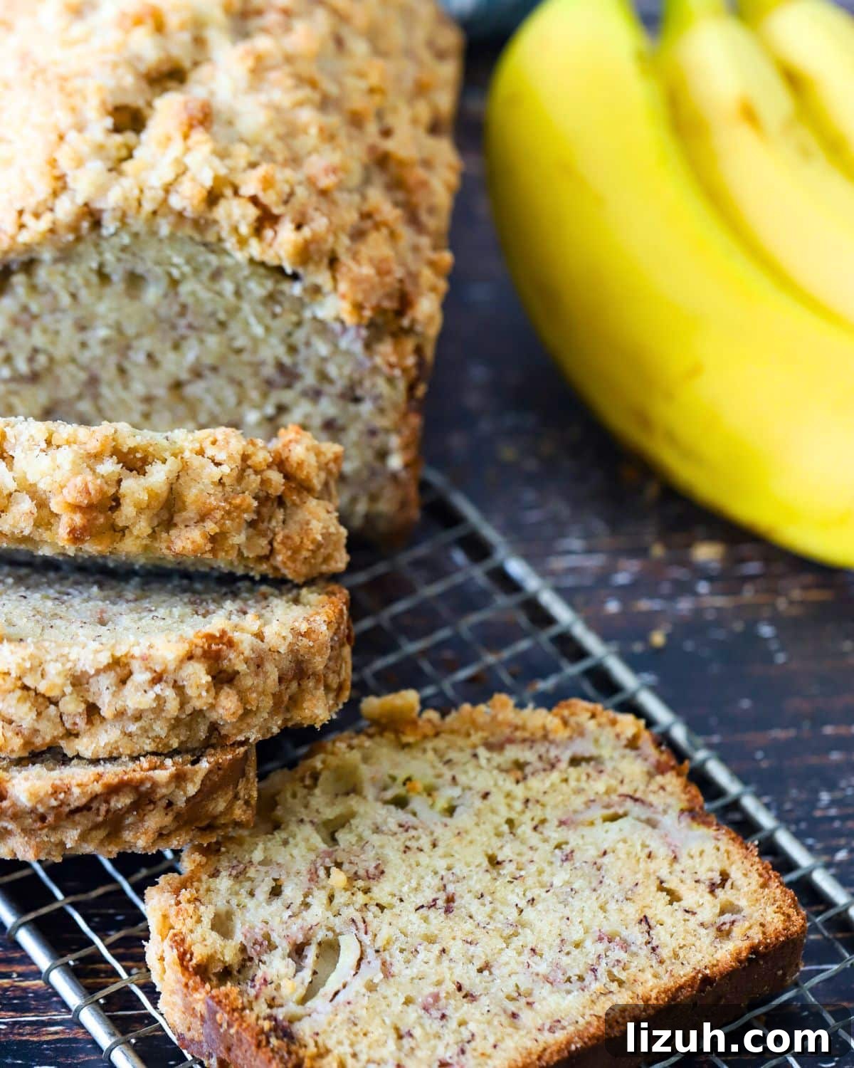 Moist Banana Bread with Crunchy Streusel Topping 12 Banana Bread on a cooling rack with a bunch of bananas next to it.
