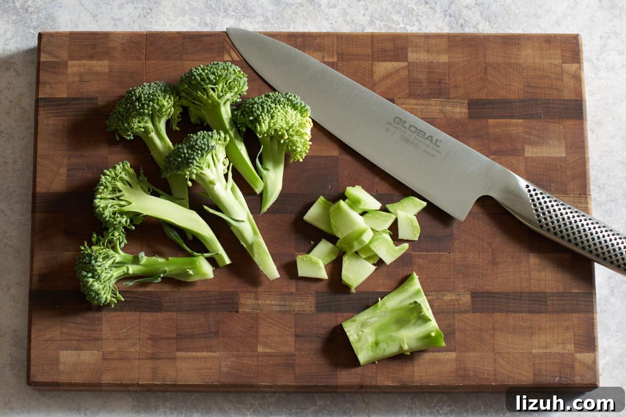 Chopped broccoli florets and stalks on a cutting board with a knife.