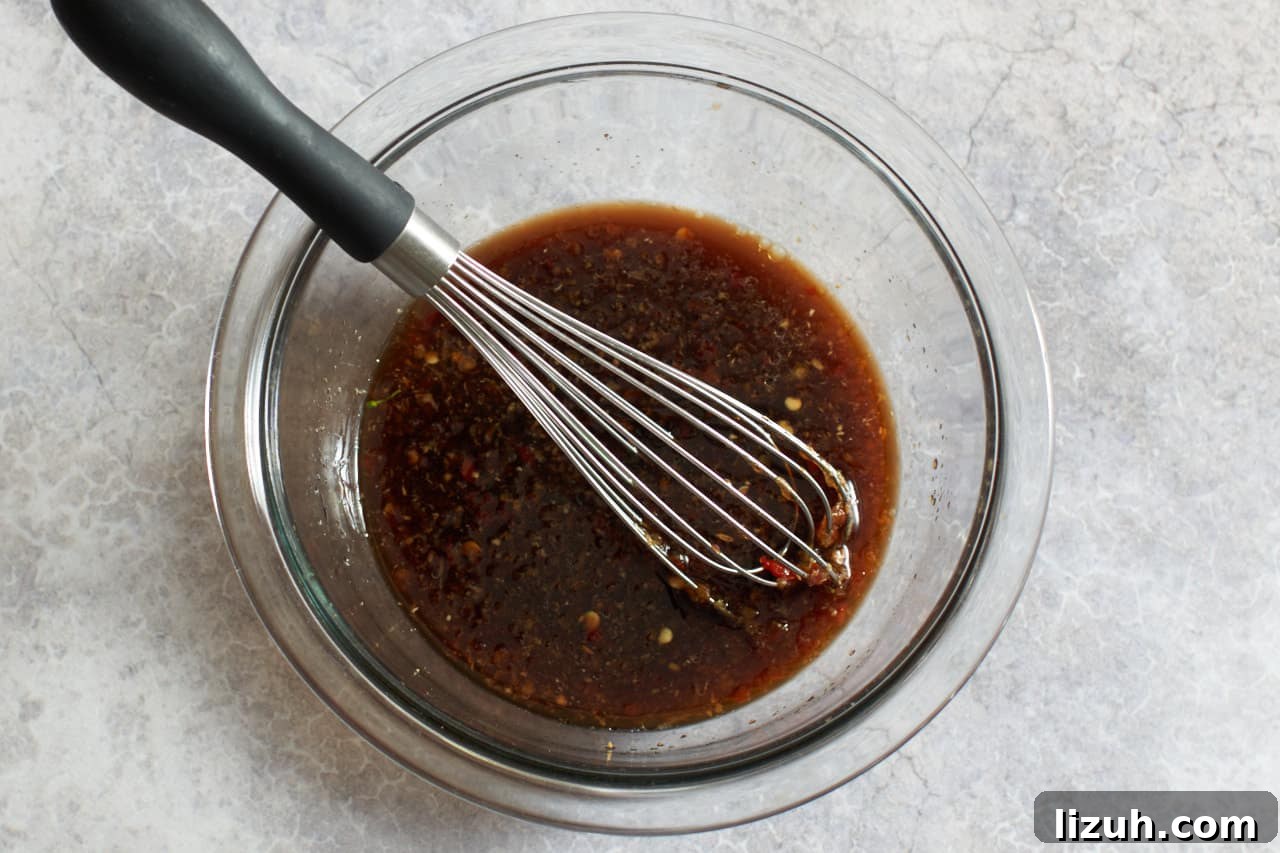 A bowl of spicy asian sauce for broccoli with a whisk in it.