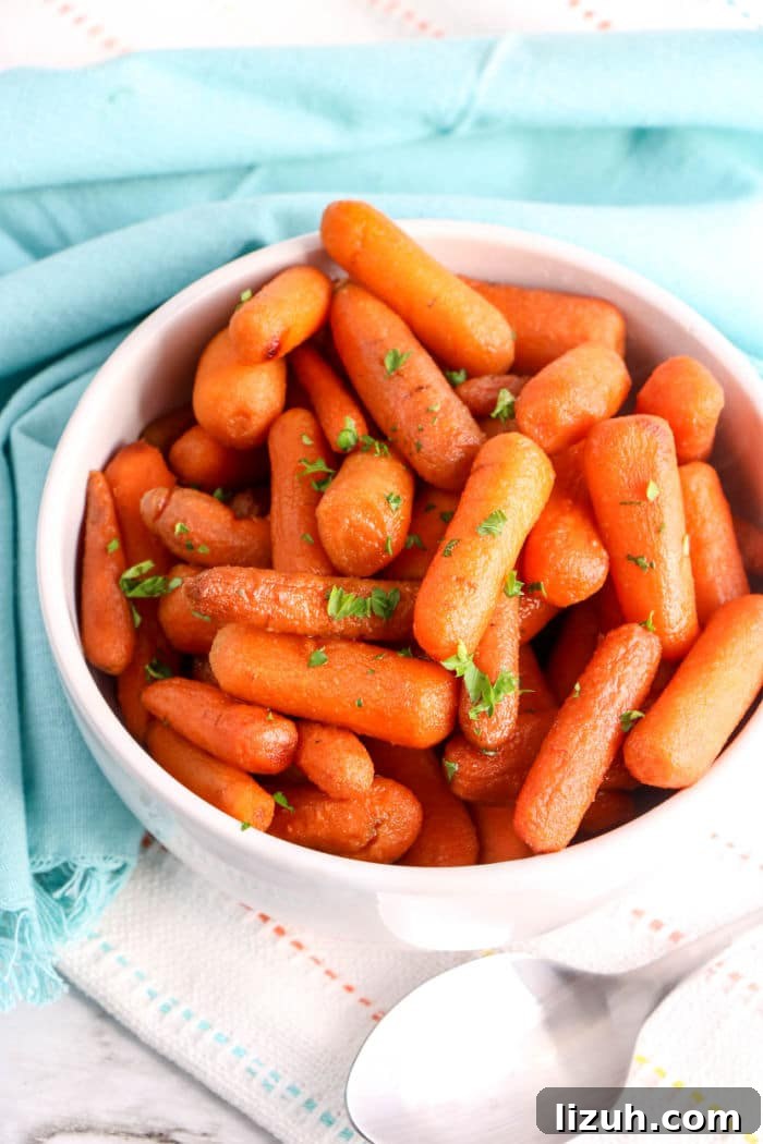 Slow-Cooked Honey-Glazed Carrots for the Crockpot 5 A bowl of tender crockpot carrots garnished with parsley sits on a blue cloth, with a spoon nearby.