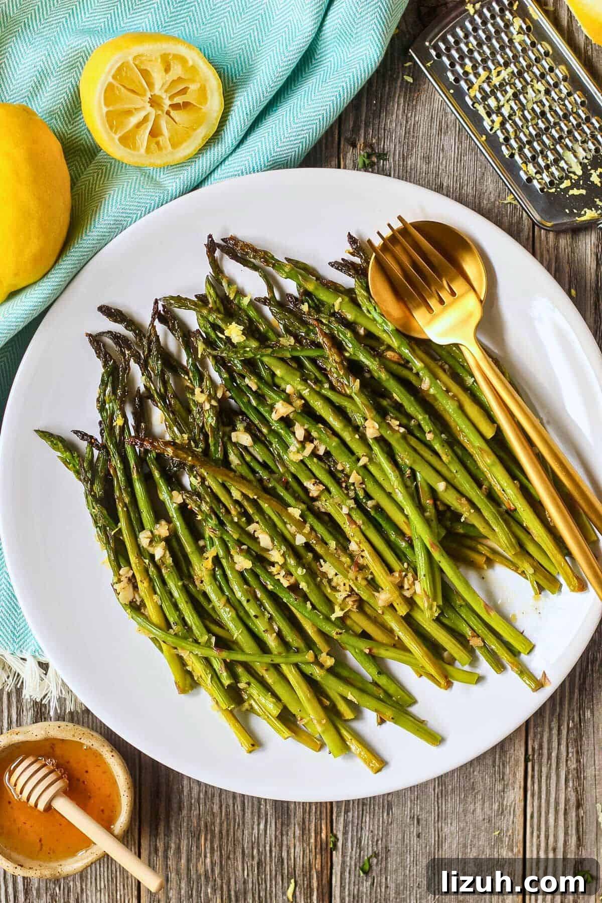 Honey lemon roasted asparagus on a white plate with a gold fork and spoon.