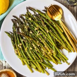 Honey lemon roasted asparagus on a white plate with a gold fork and spoon.