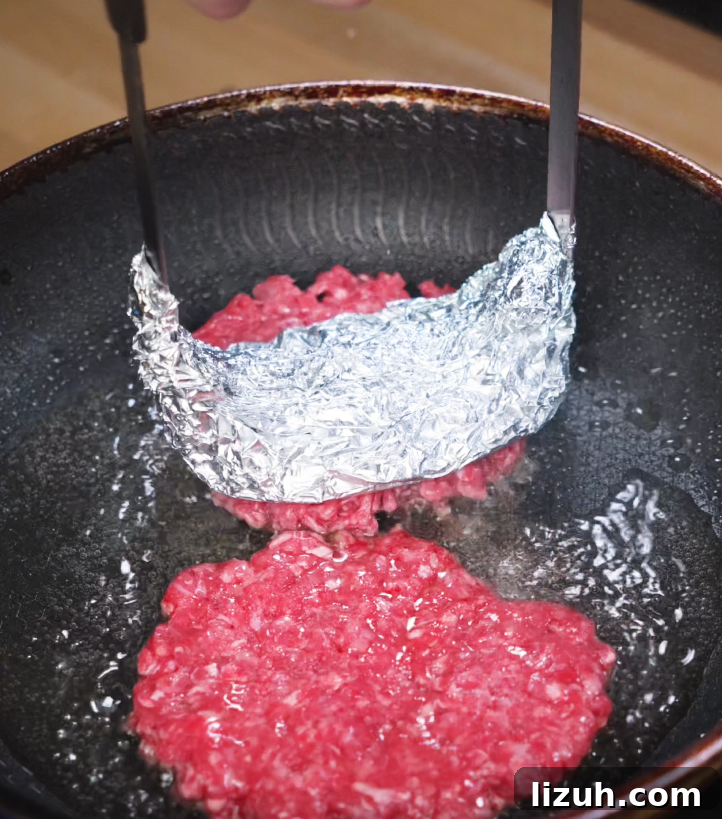 How to Make a Juicy Smash Burger at Home 5 Beef balls smashed flat with foil-wrapped spatula in a hot skillet to create crispy smash burger patties, key for the signature sear.