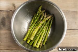 This is a picture of asparagus in a bowl with oil and seasoning.