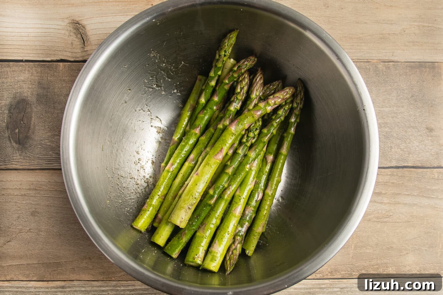 This is a picture of asparagus in a bowl with oil and seasoning.