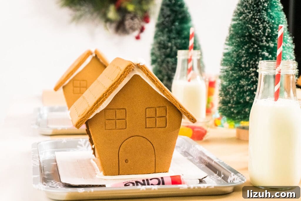 Host a Festive Gingerbread House Party: Tips, Themes & Checklist 3 premade gingerbread houses on small sheet pans with icing sugar, glasses of milk, candies and more before kids decorate