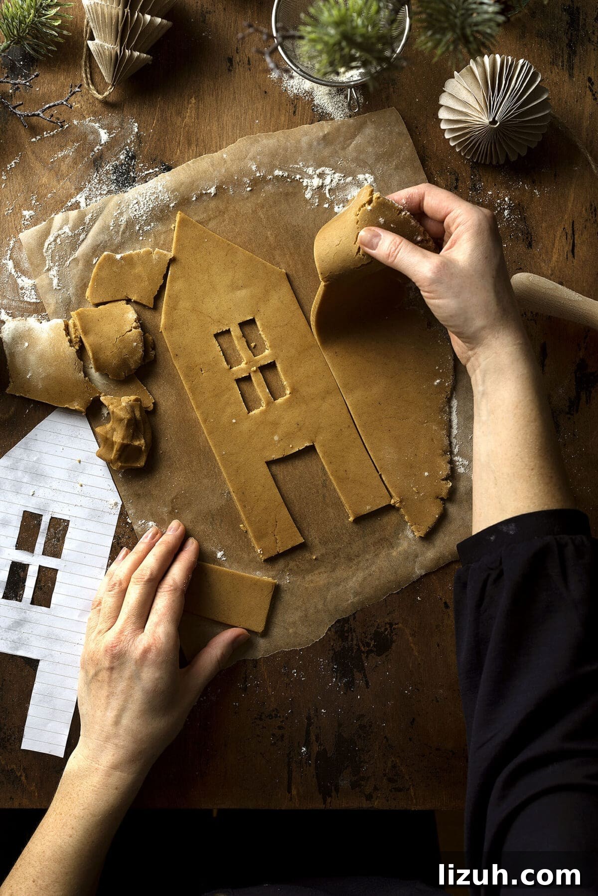 Host a Festive Gingerbread House Party: Tips, Themes & Checklist 4 a set of hands cuts out a side of a gingerbread house from cookie dough on a wooden table