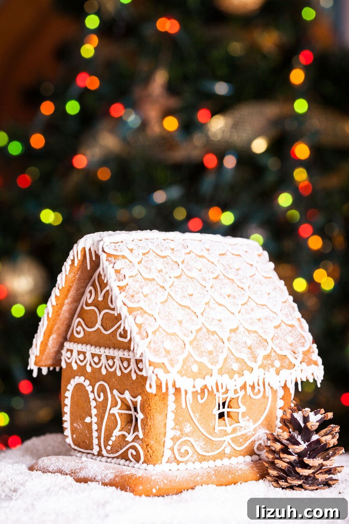 Host a Festive Gingerbread House Party: Tips, Themes & Checklist 8 A frosted gingerbread house with white icing in front of a brightly lit christmas tree