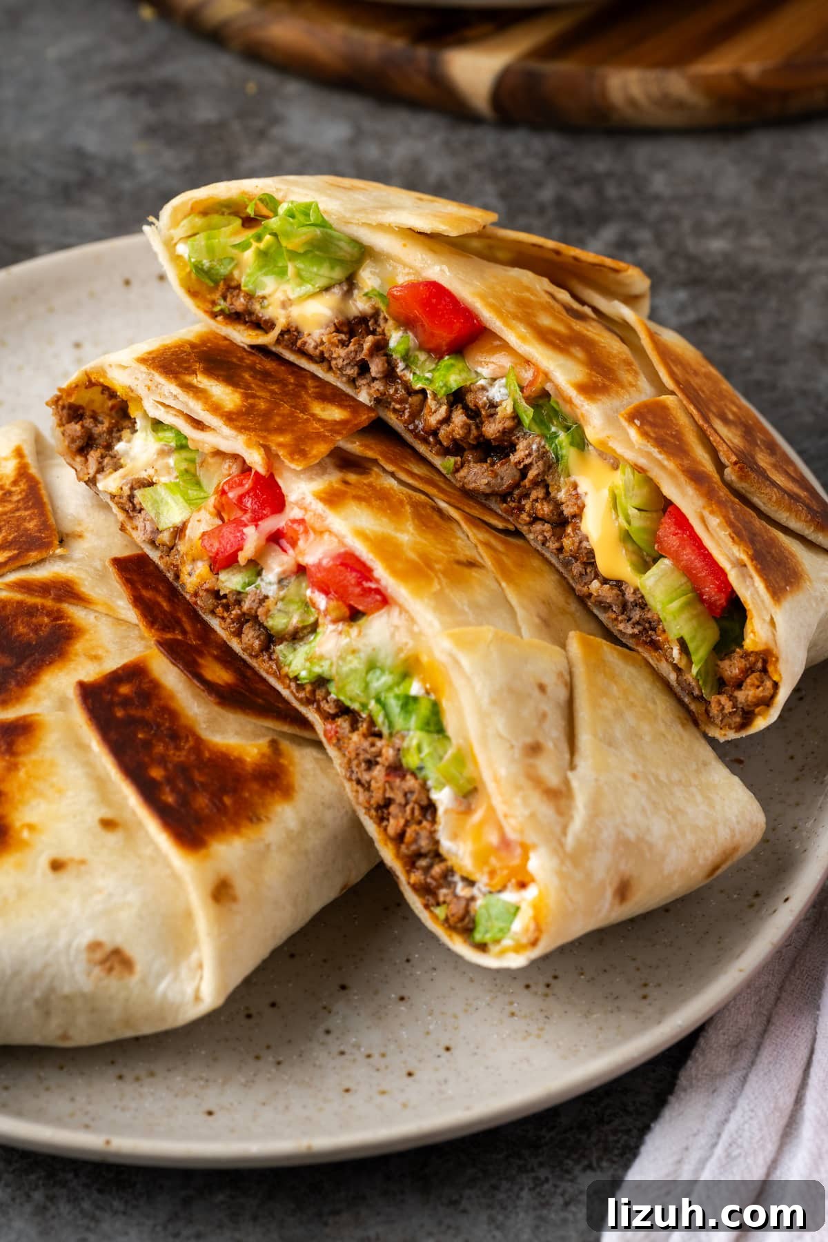 Two pan-fried crunch wraps on a plate, with one crunch wrap cut in half to reveal the layers inside.