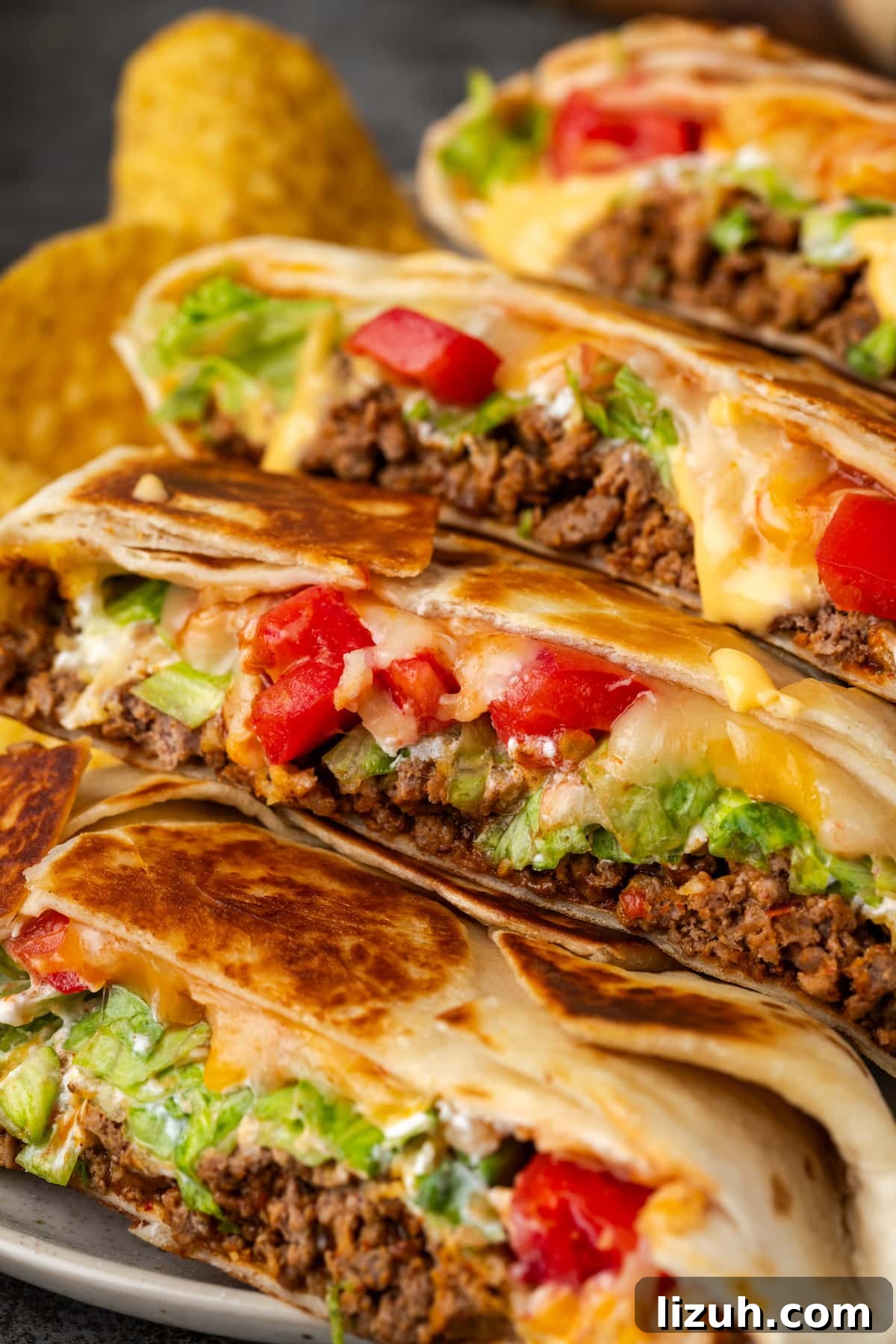 Close up of crunch wraps cut in half and arranged in a row on a plate next to corn chips.