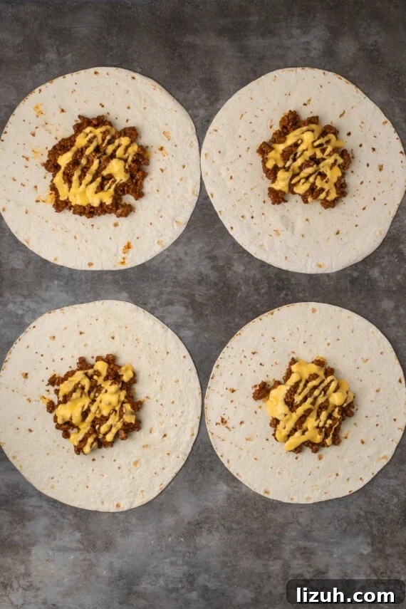 Overhead view of four partially assembled crunch wraps topped with meat and nacho cheese.