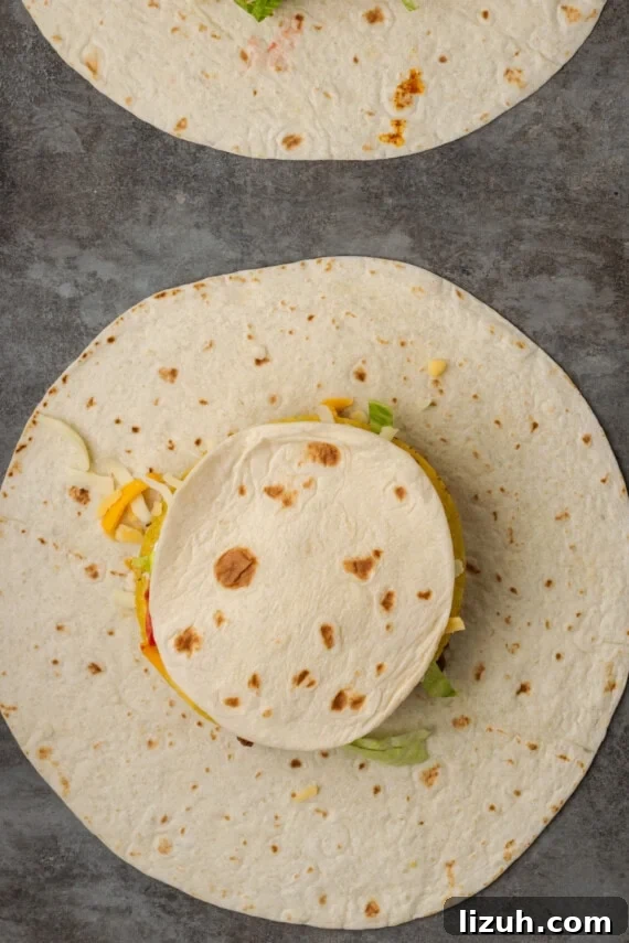 A smaller tortilla placed over the fillings of an unfolded crunch wrap.