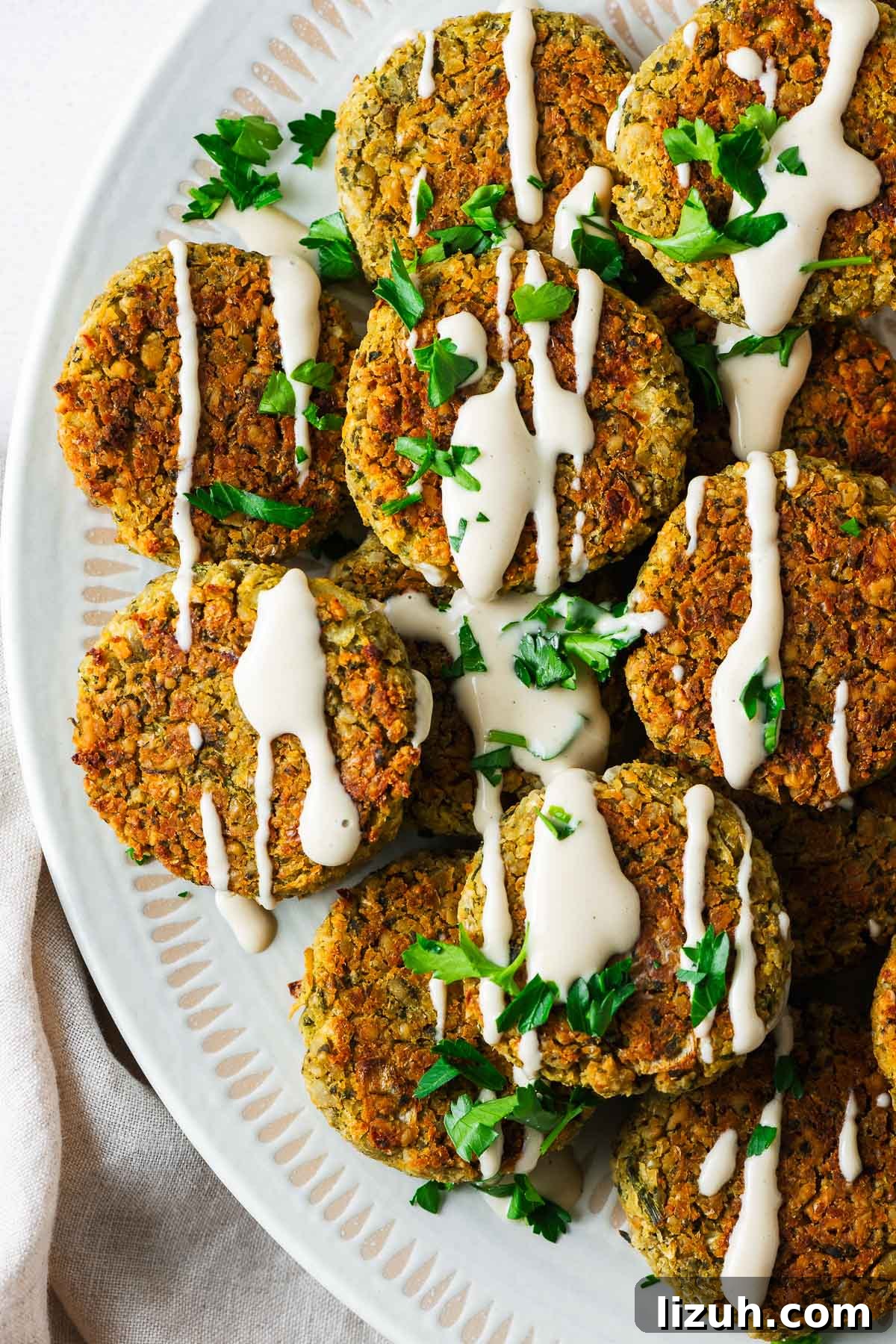 Crispy Oven-Baked Falafel Using Canned Chickpeas 2 Top down view of a serving bowl with baked falafel made with canned chickpeas drizzled with tahini sauce.