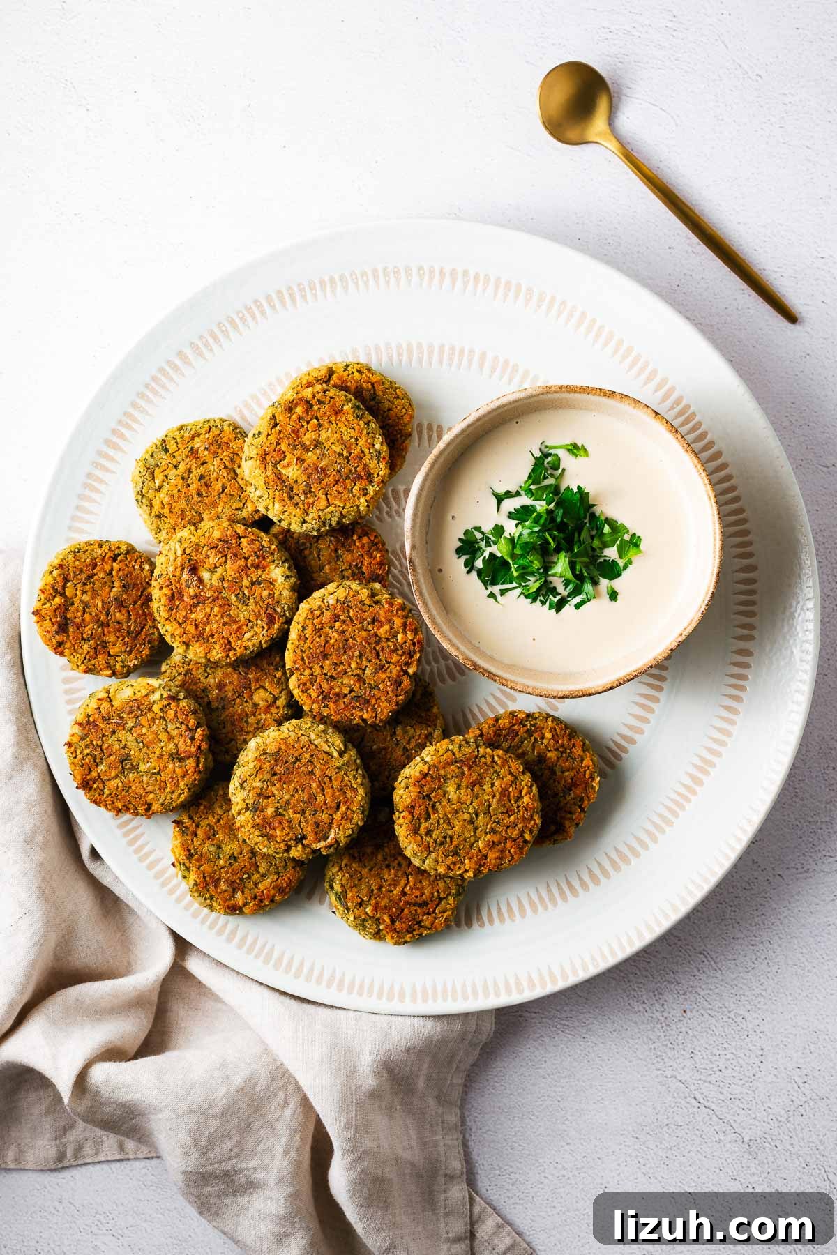Crispy Oven-Baked Falafel Using Canned Chickpeas 11 A white serving bowl with baked falafel and tahini sauce viewed from above.