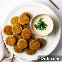 Crispy Oven-Baked Falafel Using Canned Chickpeas 12 Baked falafel patties on a white serving plate with falafel sauce in a small bowl.
