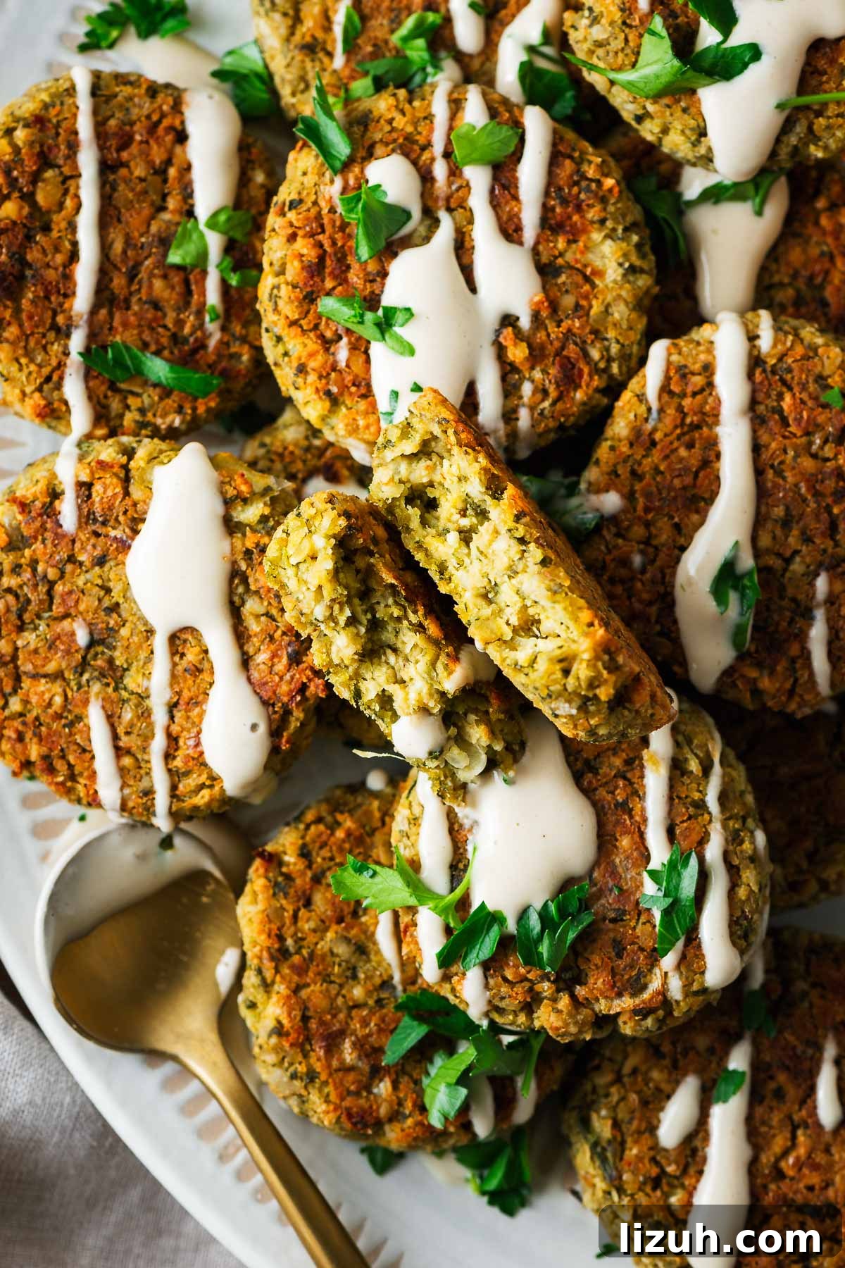 Crispy Oven-Baked Falafel Using Canned Chickpeas 3 A falafel patty broken in half to expose the texture surrounded by more whole falafel patties.
