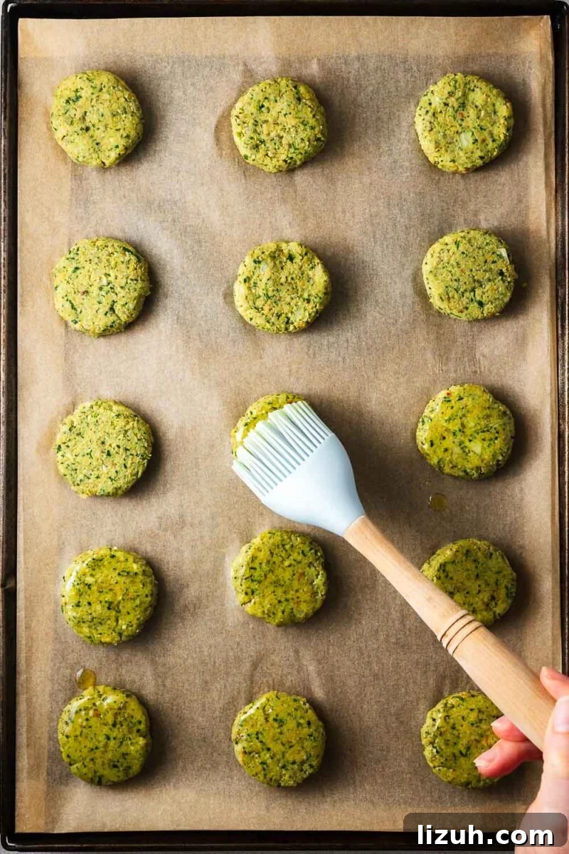 Crispy Oven-Baked Falafel Using Canned Chickpeas 9 Brushing falafel patties arranged on a parchment-lined baking sheet with olive oil.