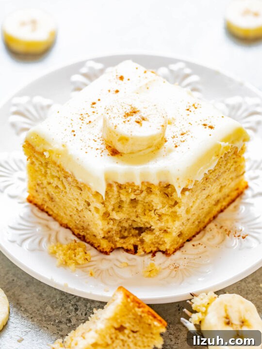 A slice of banana cake with cream cheese frosting with a bite missing.
