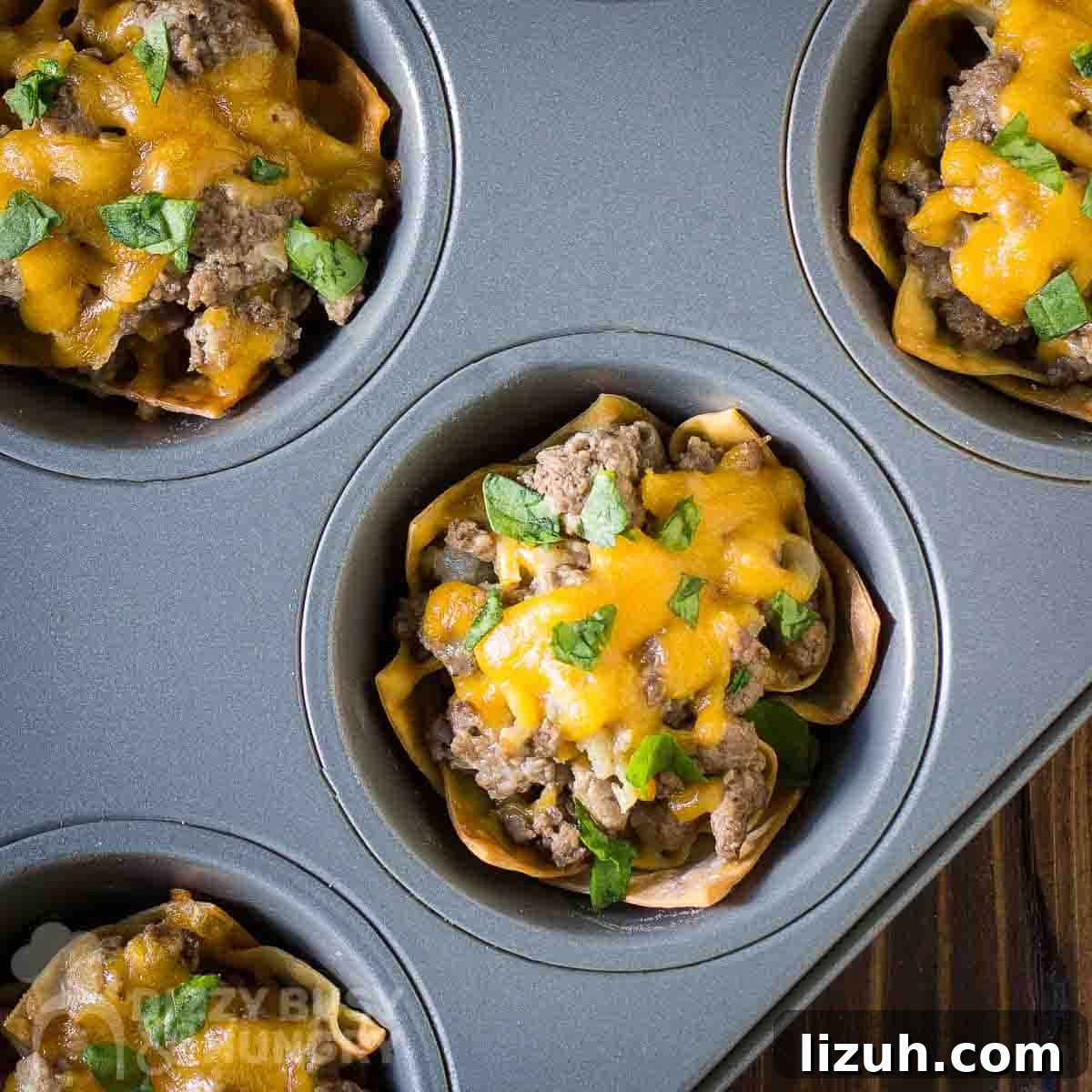 Crispy Wonton Cheeseburger Cups — Bite-Sized Party Sliders 6 Overhead shot of multiple wonton cheeseburger cups in a cupcake sheet on a wooden surface.
