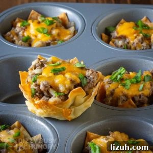 Crispy Wonton Cheeseburger Cups — Bite-Sized Party Sliders 8 Side shot of a wonton cheeseburger cup sitting on the flat part of a cupcake sheet with more in the background.