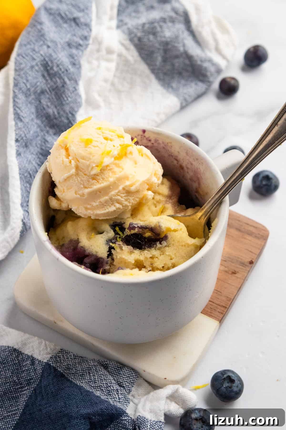 Lemon mug cake in white mug with ice cream on top.