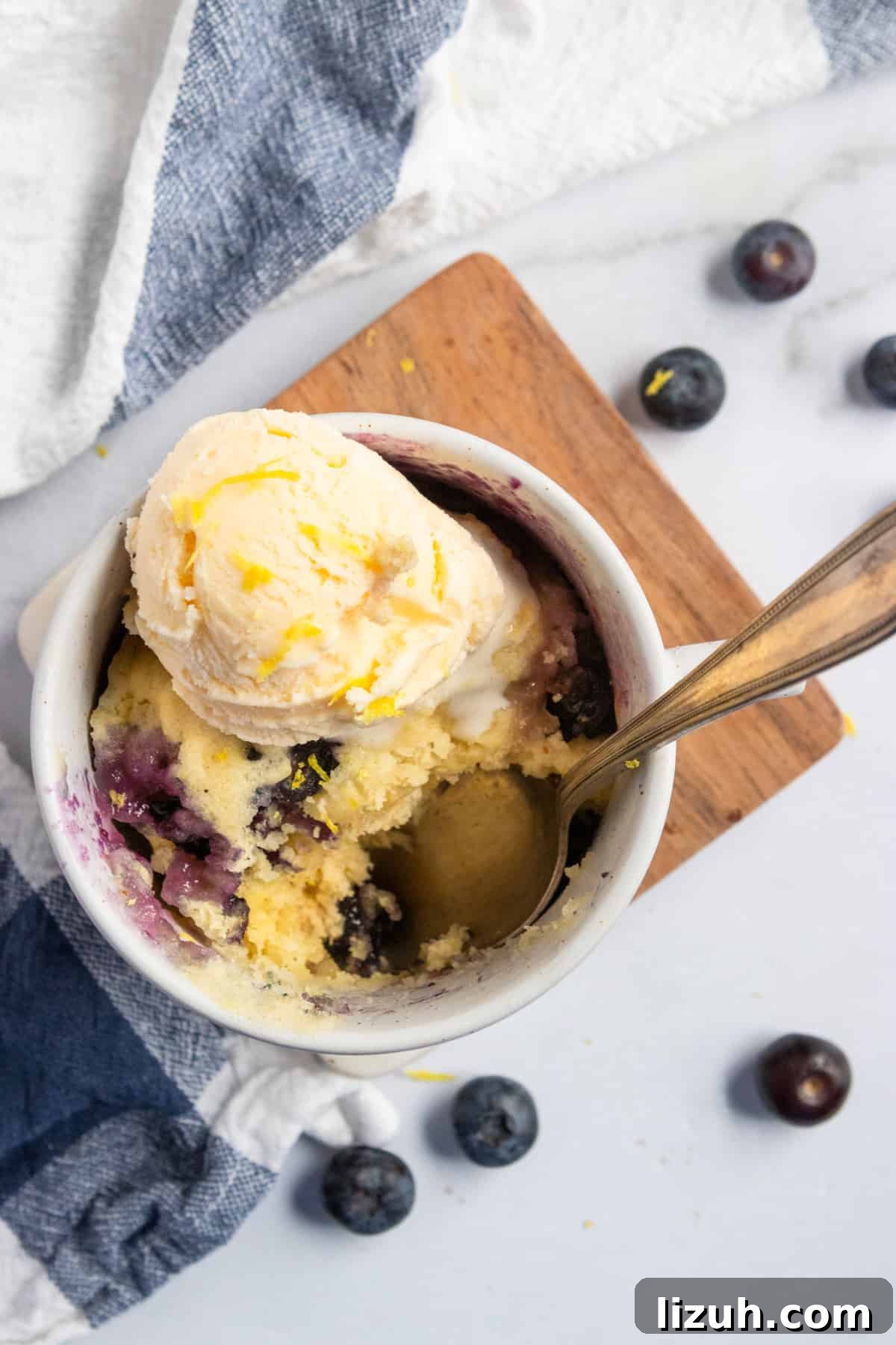 lemon cake in mug with blueberries and vanilla ice cream.
