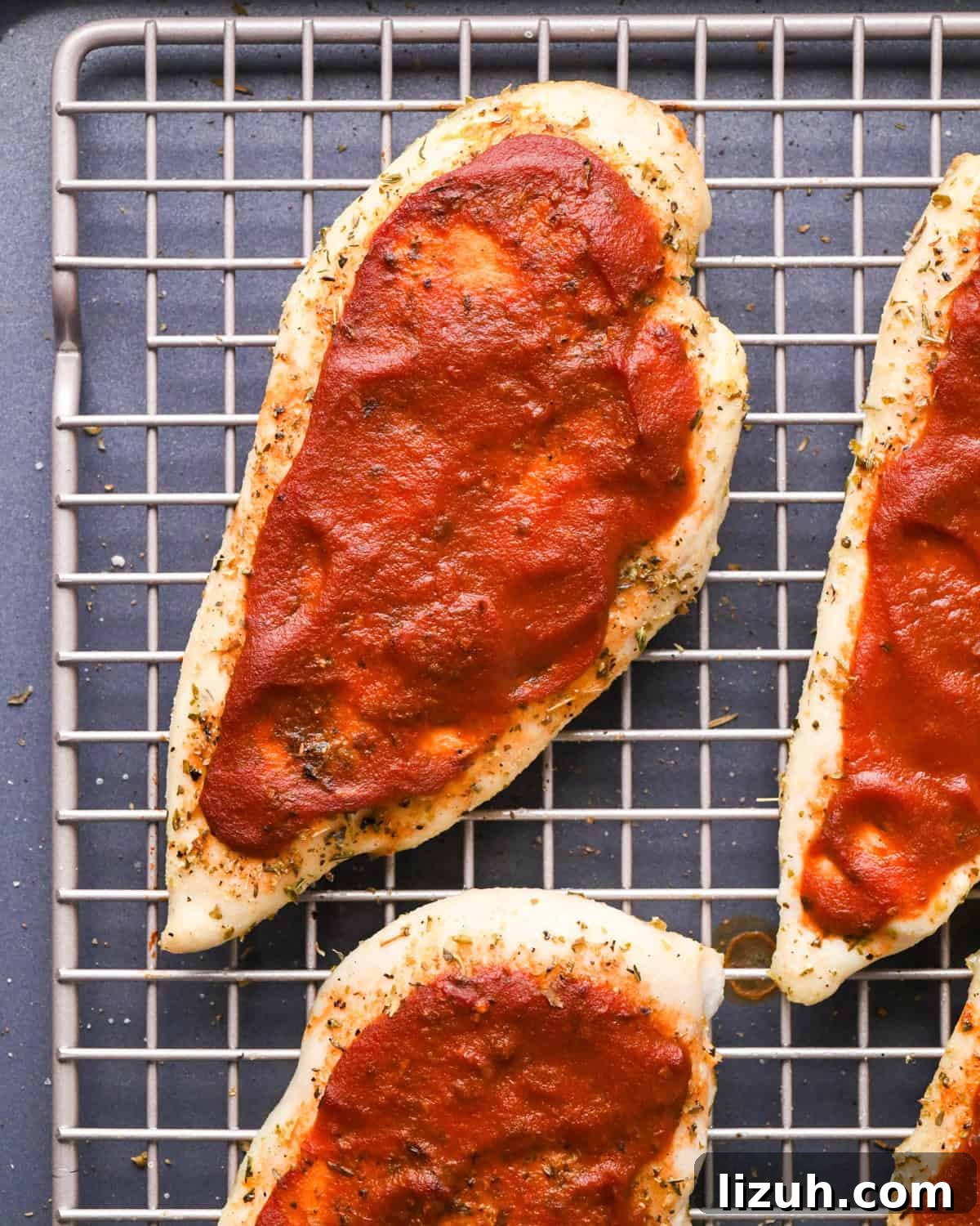 Making pizza chicken: close-up photo of chicken breasts sprinkled with spices and topped with pizza sauce.