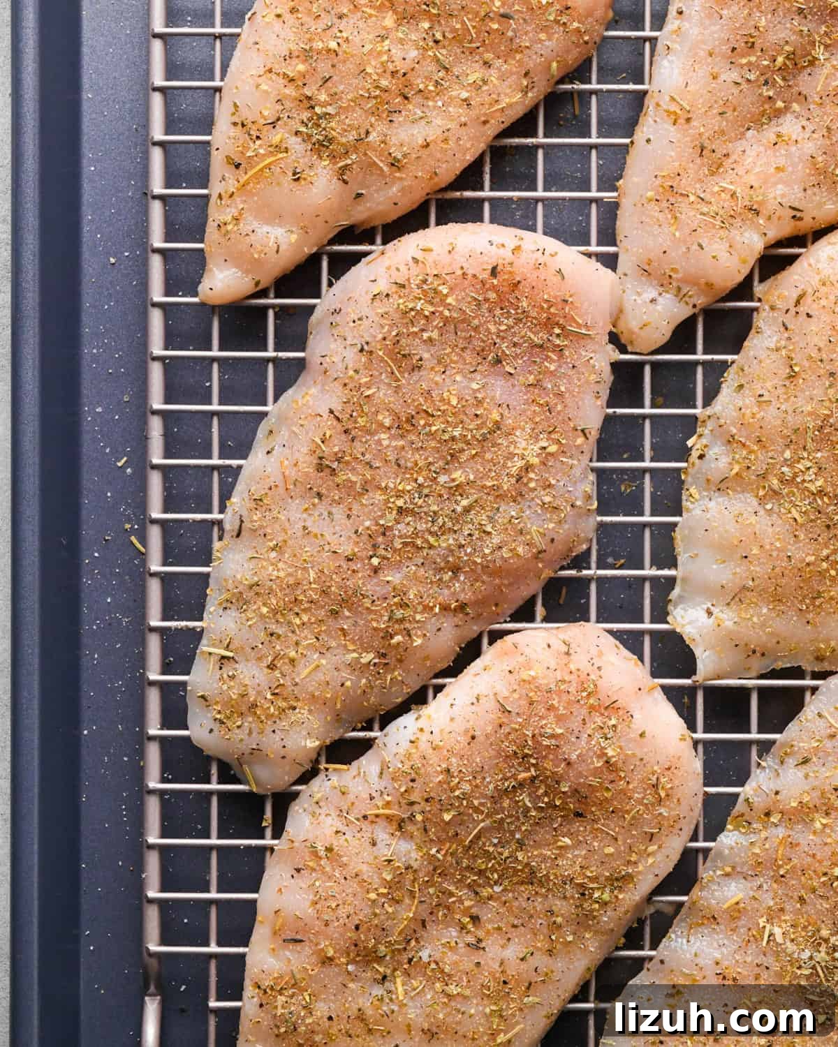 Making pizza chicken: close-up photo of chicken breasts sprinkled with spices and placed on a cooling rack on top of a baking sheet.