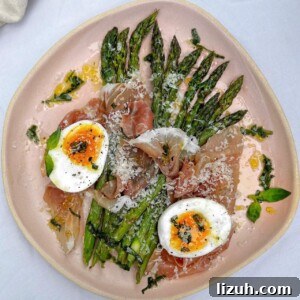 asparagus on a pink plate topped with parma ham, parmesan and a soft boiled egg